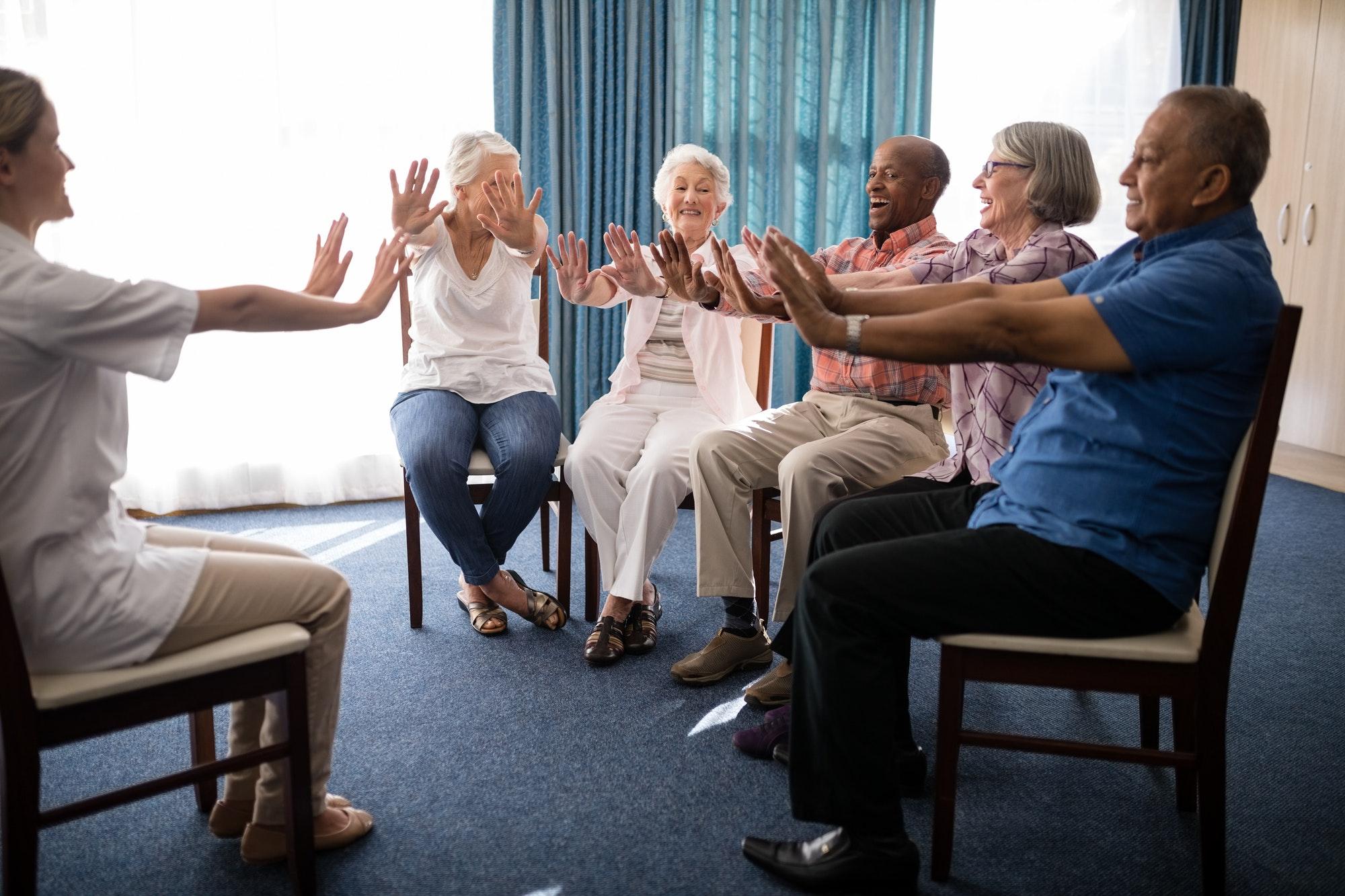 Female doctor and seniors exercising on chairs